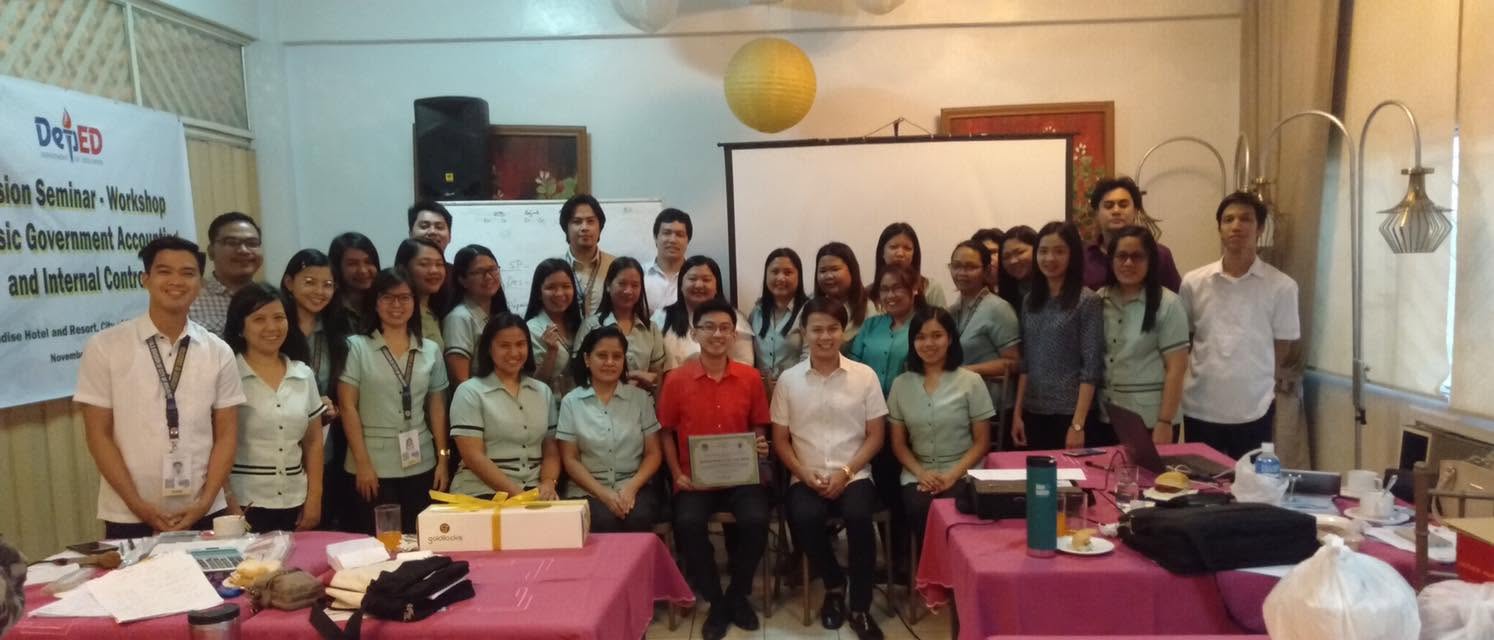 Wide group photo of DepEd Division seminar participants with Jayson holding a certificate beside the event banner