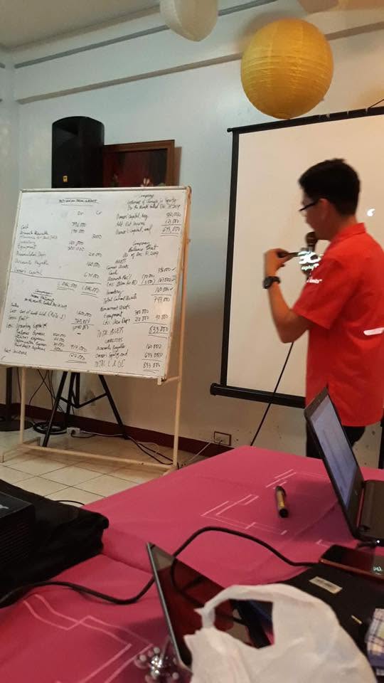 Jayson explaining a handwritten trial balance and financial statements on a whiteboard at the DepEd seminar