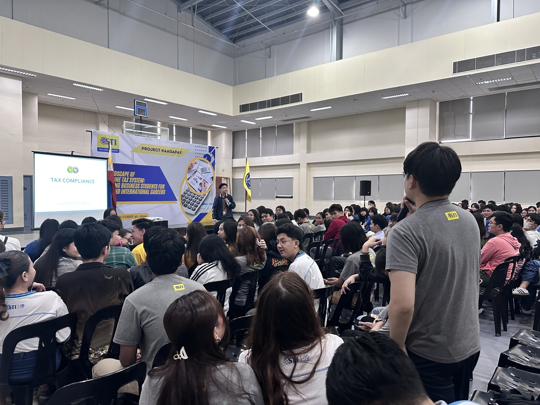 Wide view of the STI College student audience with Jayson on stage and a Tax Compliance slide projected
