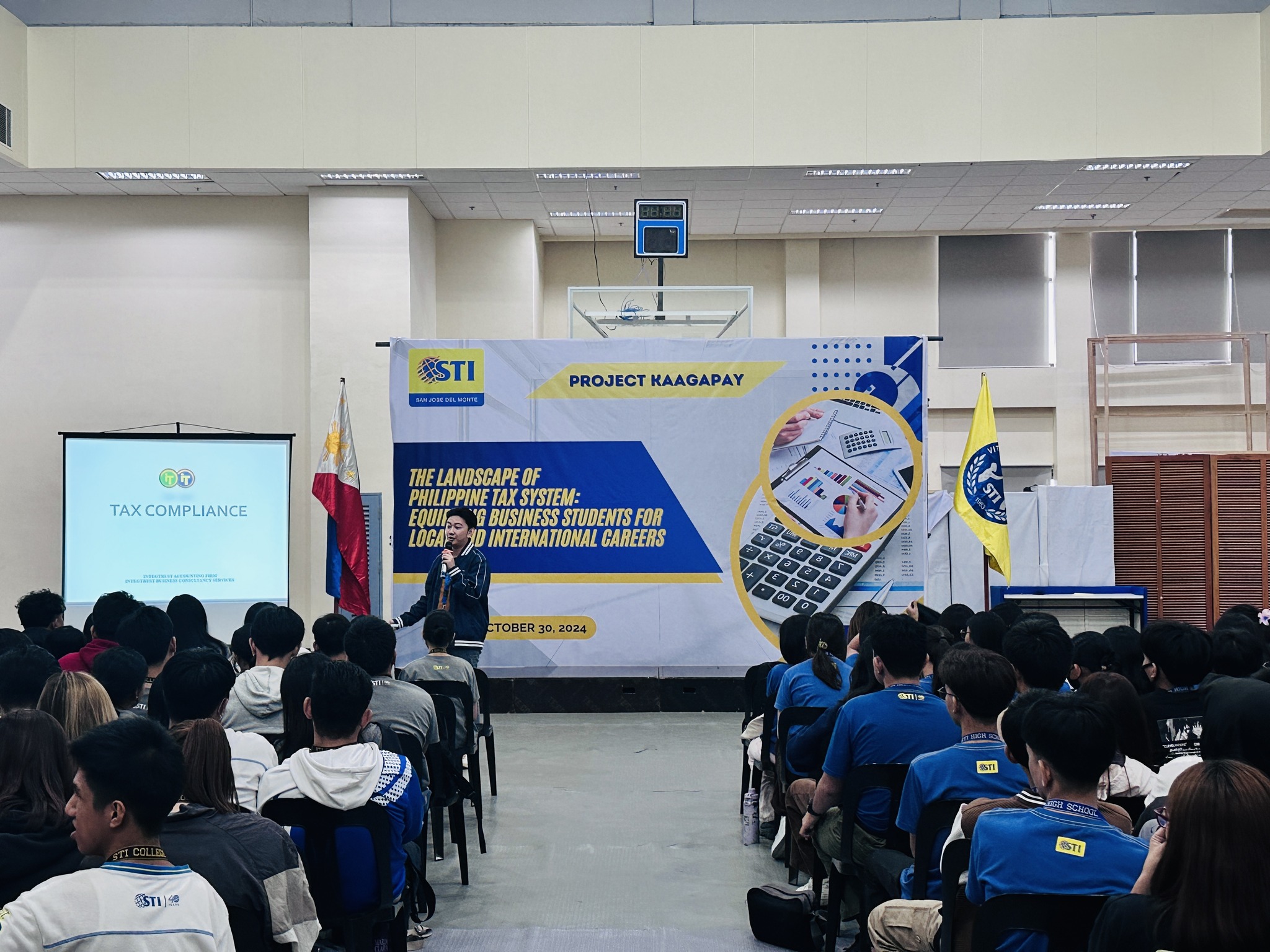 Jayson presenting the Landscape of the Philippine Tax System on stage to seated STI College students