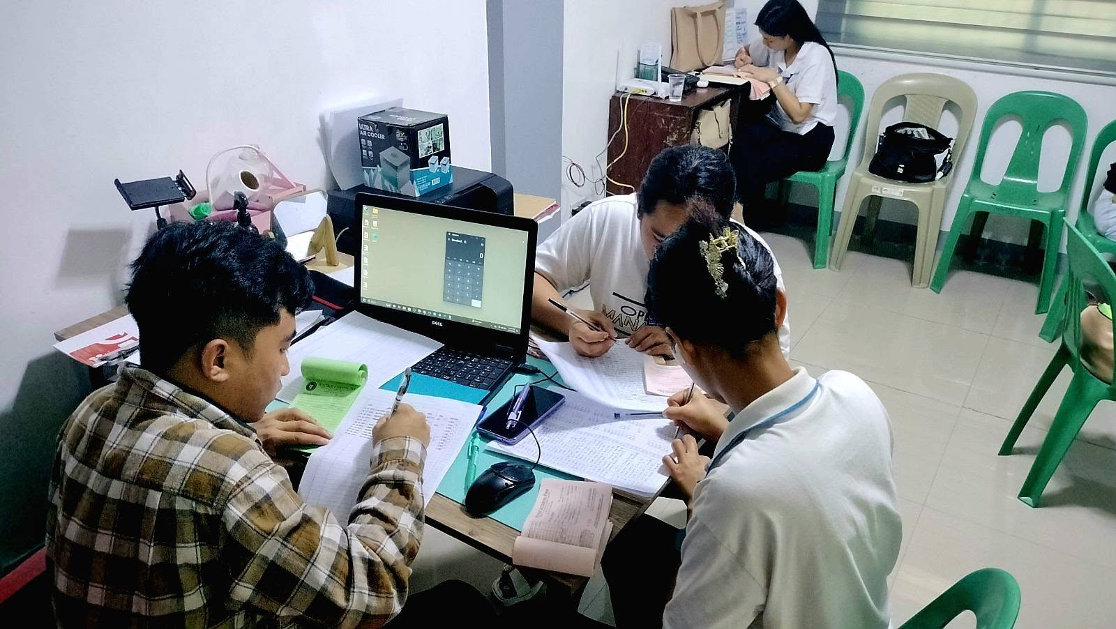 Business administration students working closely on bookkeeping exercises with a laptop and ledgers during the IntegTrust workshop